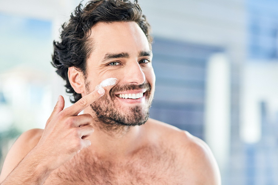 Cropped shot of a handsome young man applying moisturizer to his face inside the bathroom at home